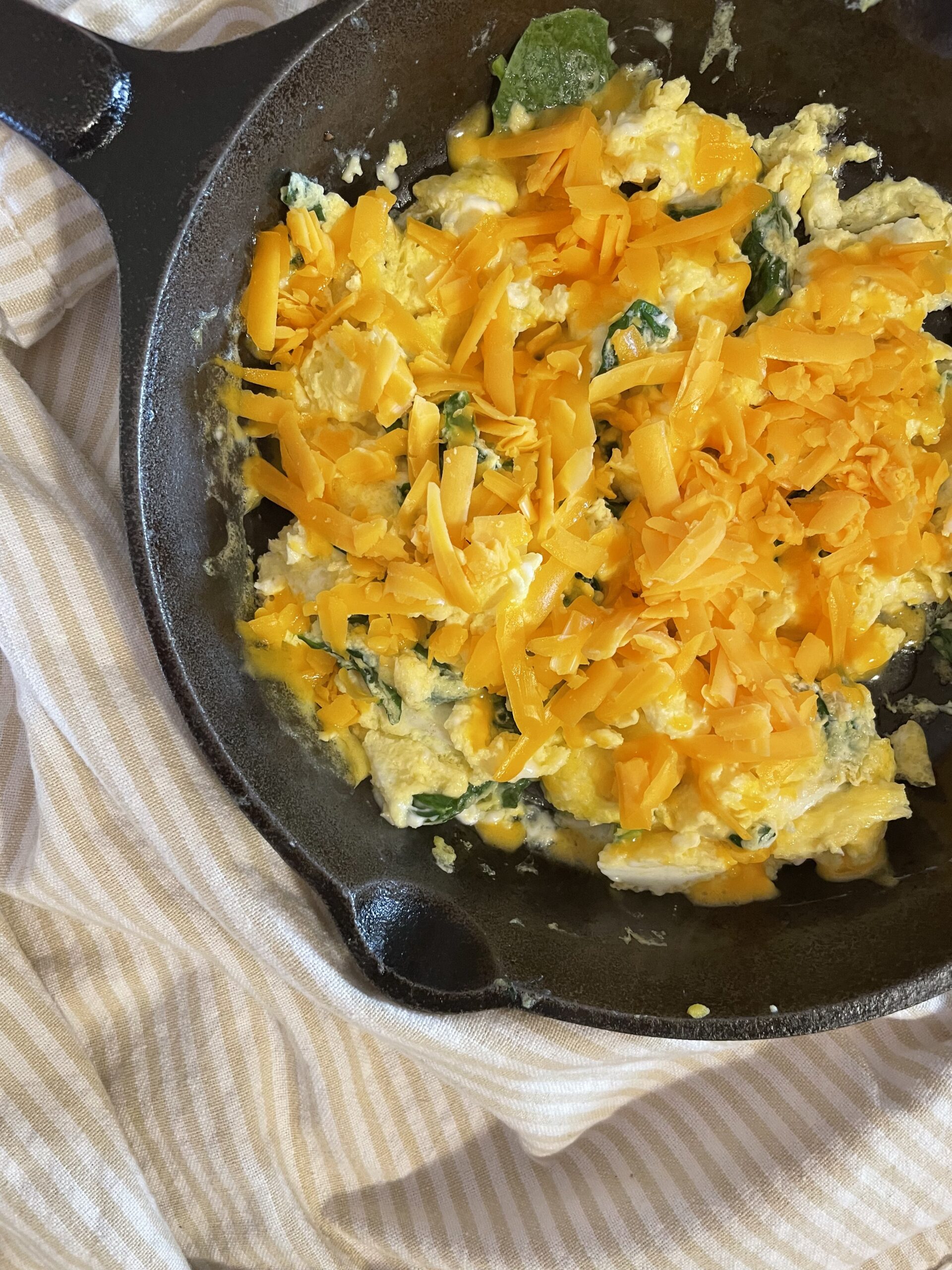 eggs and cheese in a cast iron skilled with a striped towel