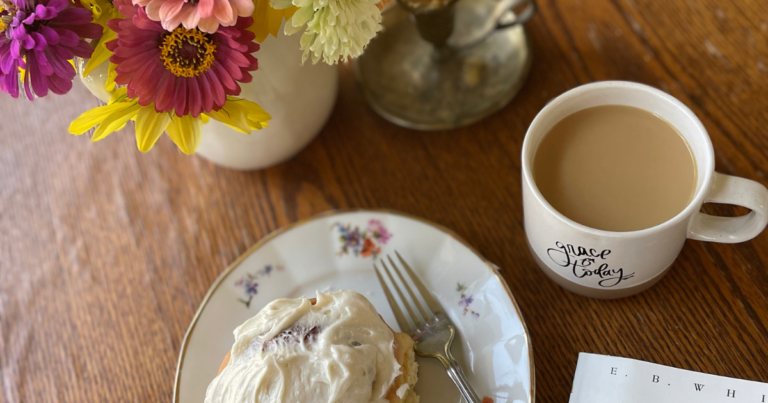 cinnamon roll on a table with flowers, coffee, and candle stick